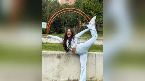 TefyRusso poses outdoors in a light blue long-sleeve crop top and matching leggings, lifting one leg high behind her head.