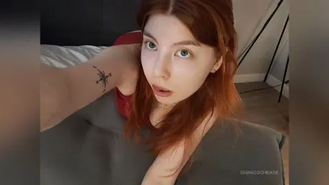 Redheaded woman with a star tattoo relaxing on a grey pillow in a cozy bedroom setting.