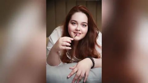 Smiling redhead woman in a white top relaxing indoors with a playful and cozy mood.