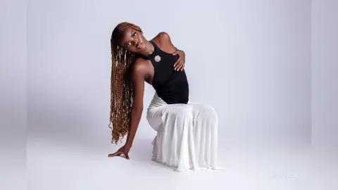 Elegant Black woman in a black halter top and white flowing skirt posing gracefully against a white background.