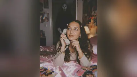 Young woman in a cozy bedroom talking on a vintage landline phone with a spooky Ghostface figure in the background.