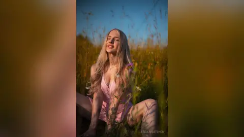 StellaFletcher sits in a grassy field wearing a pink lace bodysuit with her eyes closed.