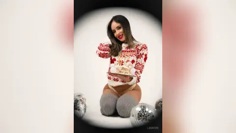 Smiling woman in festive red Christmas sweater holding a cake in a bright holiday setting.