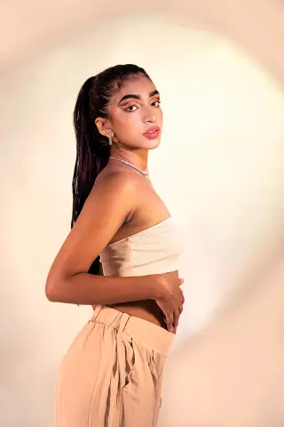 Veronica_Hottiee poses sideways in a tan tube top and matching tan pants against a plain light background.