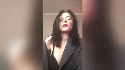 Stylish woman in a black top and blazer wearing round glasses with a confident mood in a minimalist setting.
