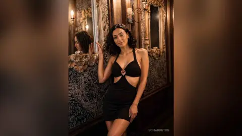 Elegant woman in a black cutout cocktail dress posing in a vintage luxury room with ornate gold mirrors.