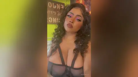 BossyBella — BossyBella poses in a black sheer bra, showing off her long curly hair and heavy pink eye makeup.