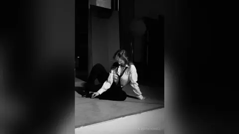 AlbertaCorrell sits on the floor in a white button-down shirt and black pants, looking down with her hair falling over her face.