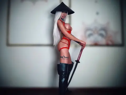 Blonde female samurai in red lingerie and black boots holding a katana in a moody indoor setting.