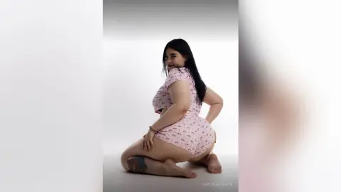 Curvy woman in pink patterned loungewear posing confidently against a white studio background.