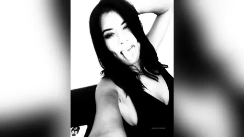SandraMidnight sticks out her tongue while wearing a black tank top and posing with one arm raised.