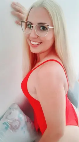 Smiling blonde woman in a red tank top posing against a white wall in a bright, cheerful mood.