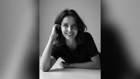 Smiling young woman in a black t-shirt posing in a minimalist indoor setting, black and white portrait.