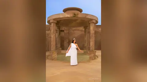 JuliahLewis stands in a stone rotunda wearing a long white sleeveless dress.