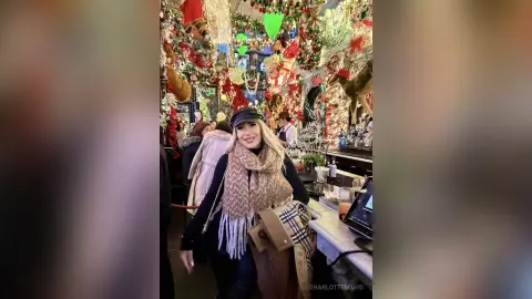 Smiling woman in a warm scarf and black hat enjoying a festive holiday atmosphere at a decorated Christmas market.