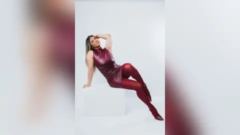 Elegant woman in a burgundy satin dress and tights posing confidently against a white studio background.