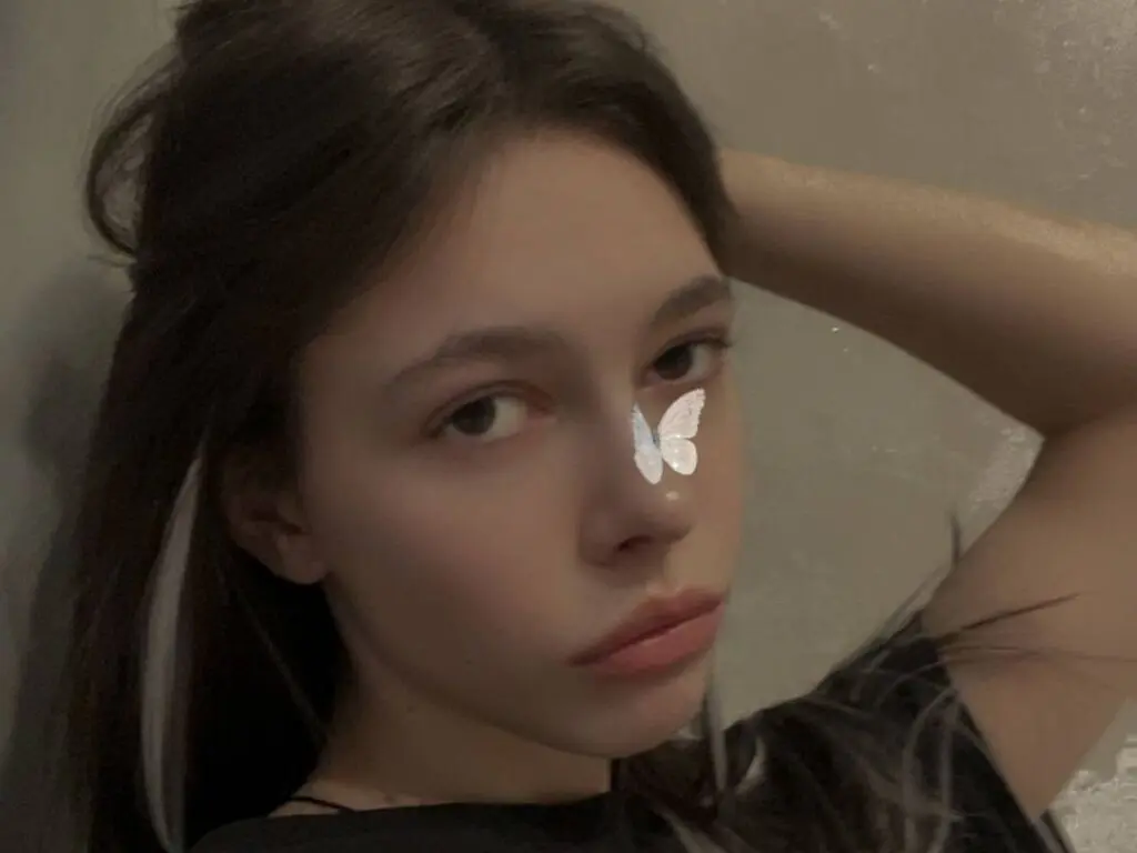 LueKottke poses with a white butterfly sticker on her nose, looking into the camera with her hand behind her head.