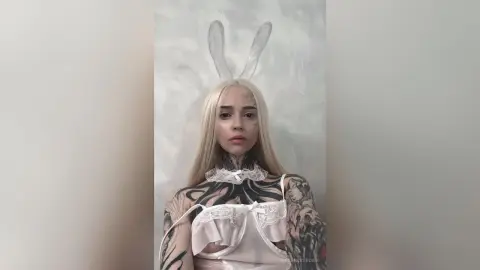 Blonde woman in white lace lingerie and bunny ears posing with a moody, artistic aesthetic.