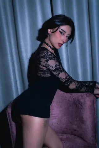 Moody portrait of a woman in a black lace long-sleeve dress sitting on a pink velvet chair.