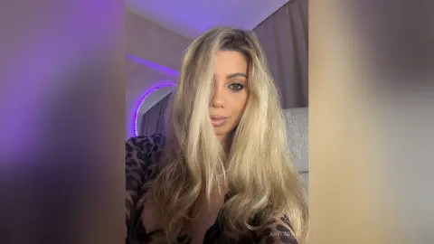 Blonde woman in a black leopard print top posing in a room with purple ambient lighting.