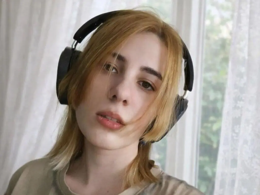 Blonde woman wearing black headphones in a bright, airy room with soft natural lighting.