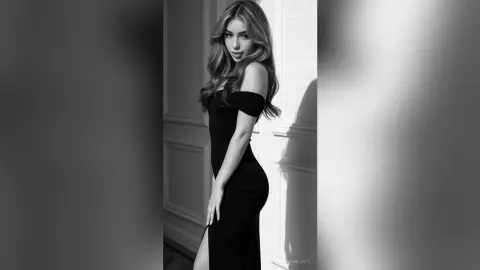 MeganLewit posing in a tight black dress with her long hair down, looking at the camera in a black and white studio setting.