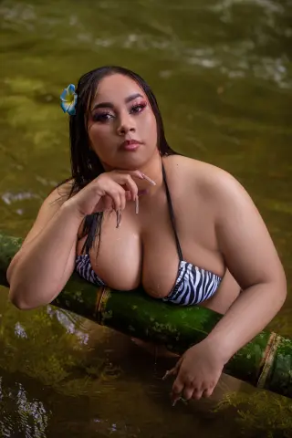 ThaliaBrookss — Curvy woman in a black and white bikini relaxing in a tropical jungle pond with a blue flower in her hair.