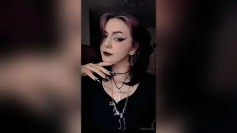 LorenLoiss poses with a hand to her chin, wearing heavy winged eyeliner and black gothic jewelry.