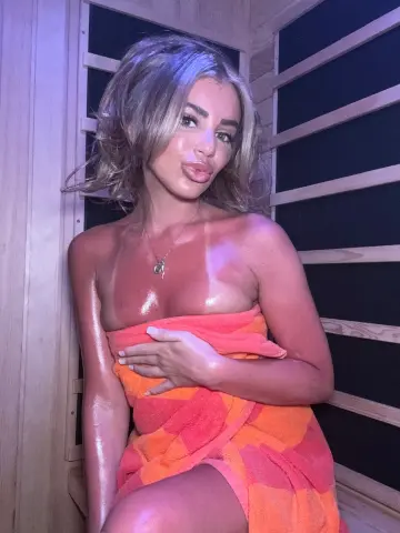 Sweaty young woman in an orange towel relaxing in a wooden sauna with a glowing skin look.