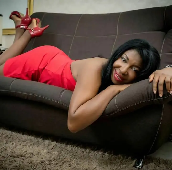 Ebonyhotxxx — Ebonyhotxxx lies on a dark brown couch wearing a tight red dress and red high heels.