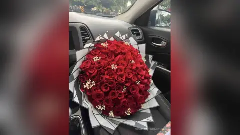Large bouquet of red roses wrapped in grey paper sitting on a car seat for a romantic gift delivery.