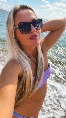 Blonde woman in pink leopard print bikini relaxing on a sunny beach by the ocean waves.