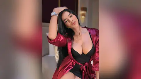 Alison poses in a black bodysuit and a shiny red satin robe, running her hand through her long black hair.