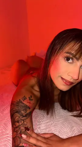 Young woman with tattoos relaxing on a white bed under warm red ambient lighting.