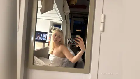 KeilaTouchton takes a mirror selfie wearing a white top while sitting on her bed.