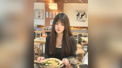 TessaMabel — TessaMabel sits at a restaurant table with long brown hair, wearing a black long-sleeved top and looking at the camera.