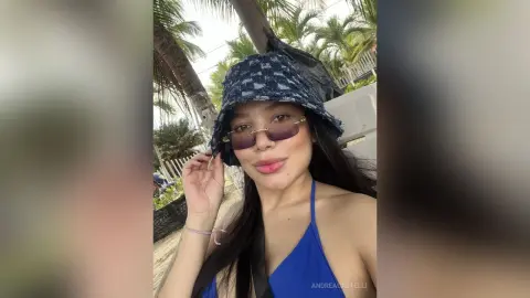 Smiling woman in a blue bikini and patterned bucket hat enjoying a sunny tropical vacation outdoors.