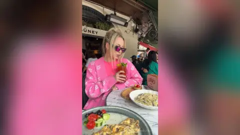 Blonde woman in a pink sweatshirt enjoying a meal and drink at an outdoor cafe terrace.