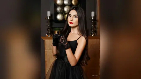 Elegant woman in a black evening gown and lace gloves posing in a moody, sophisticated indoor setting.