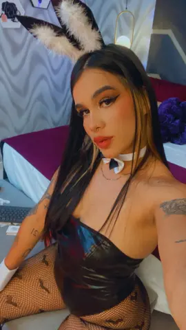 Woman in bunny ears and black corset outfit posing in a bedroom setting with a playful mood.