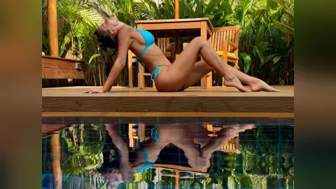 AnaMathers poses naked or in a blue bikini on a wooden deck beside a pool, arching her back with her head tilted back.