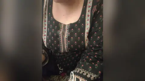 Woman in a black floral print long-sleeve tunic with traditional embroidery in a soft indoor setting.