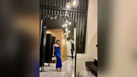 Elegant woman in a sleek blue evening gown posing in a modern luxury hotel lobby with warm lighting.