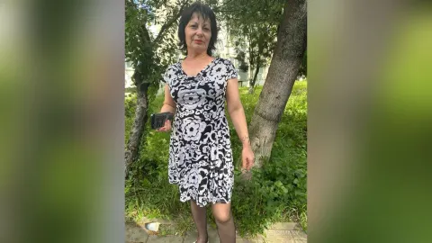 JesicaMaily — JesicaMaily stands outdoors in a black and white floral print dress holding a phone.