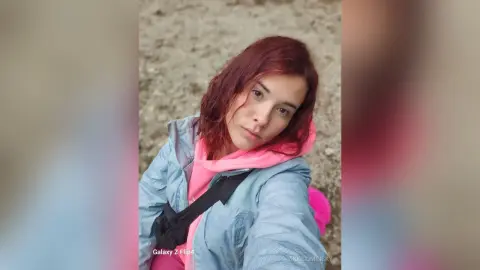 VikkiCominsky wears a pink hoodie and a light blue jacket while looking directly at the camera.