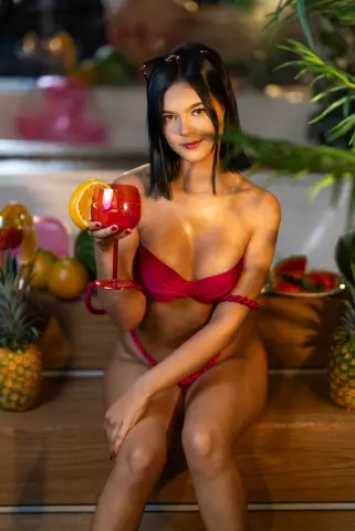 Young woman in a red bikini holding a cocktail glass at a tropical summer beach party.