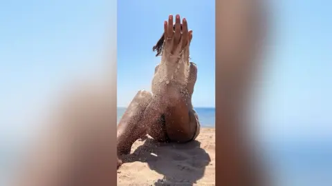 Young woman in a black bikini relaxing on a sunny beach with sand on her skin.