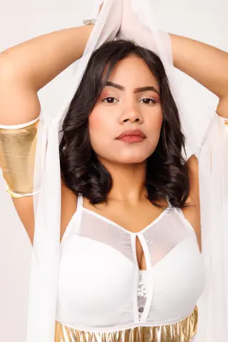 Young woman in white and gold ethereal outfit posing with flowing fabric against a soft studio background.