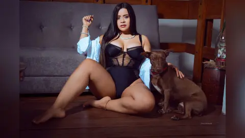 Curvy woman in black lace bodysuit and white shirt sitting on floor with a brown dog in a cozy living room.