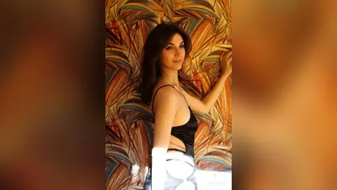 Elegant woman in a black sleeveless bodysuit posing against a tropical leaf patterned background.